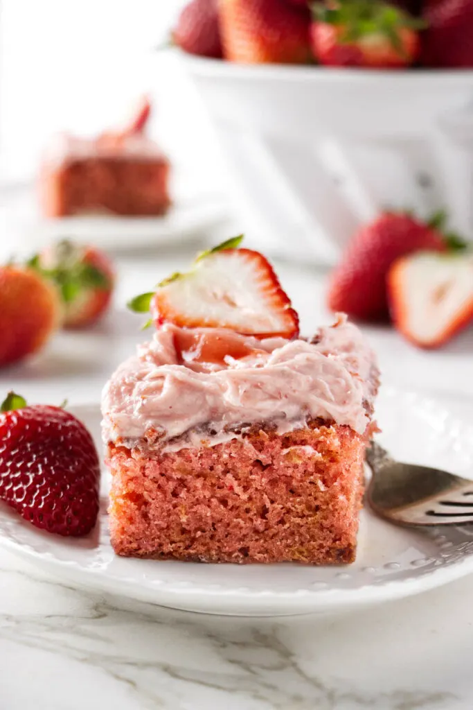 A slice of strawberry jam cake next to a fork and fresh strawberries.