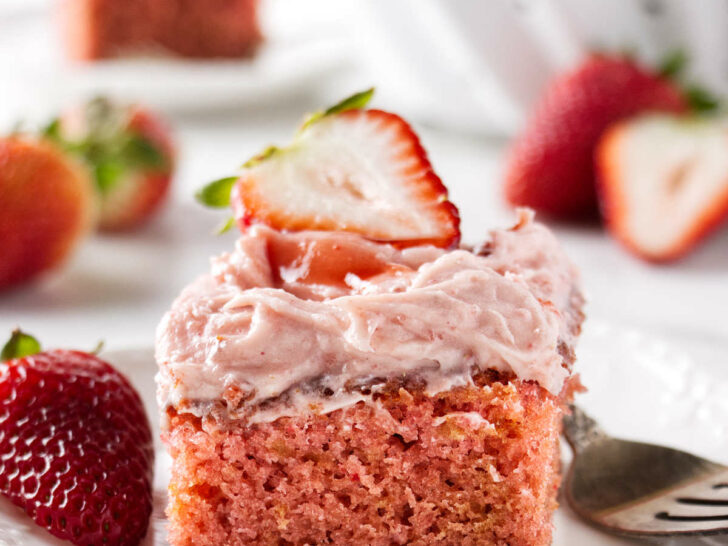 A slice of strawberry jam cake next to a fork and fresh strawberries.