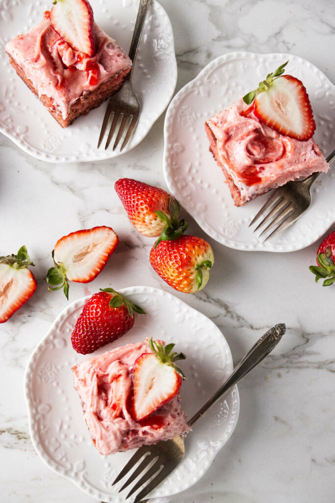 Three square slices of strawberry jam cake next to fresh strawberries.