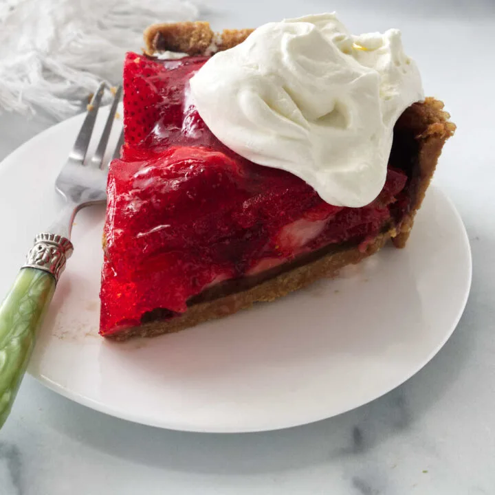 A slice of strawberry jello pie in a graham cracker crust with a layer of chocolate on the crust.