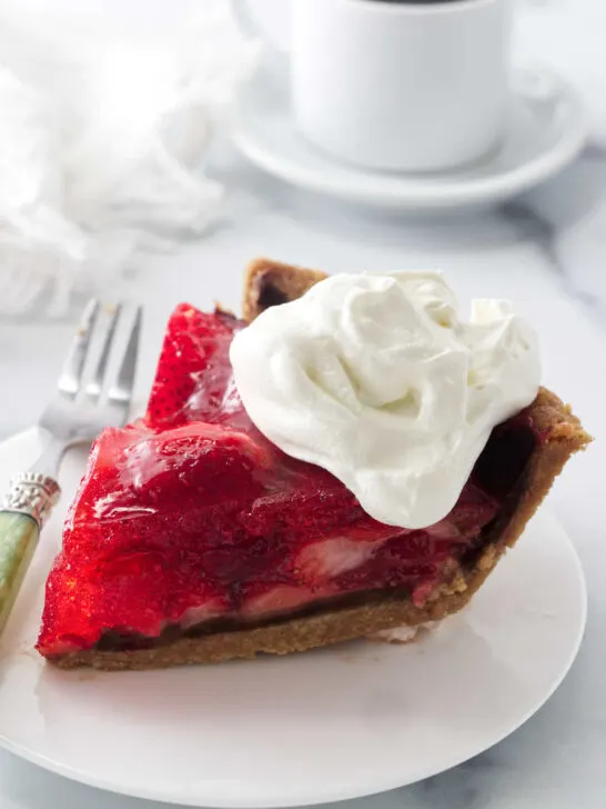 A slice of strawberry pie made with jello in front of a cup of coffee.