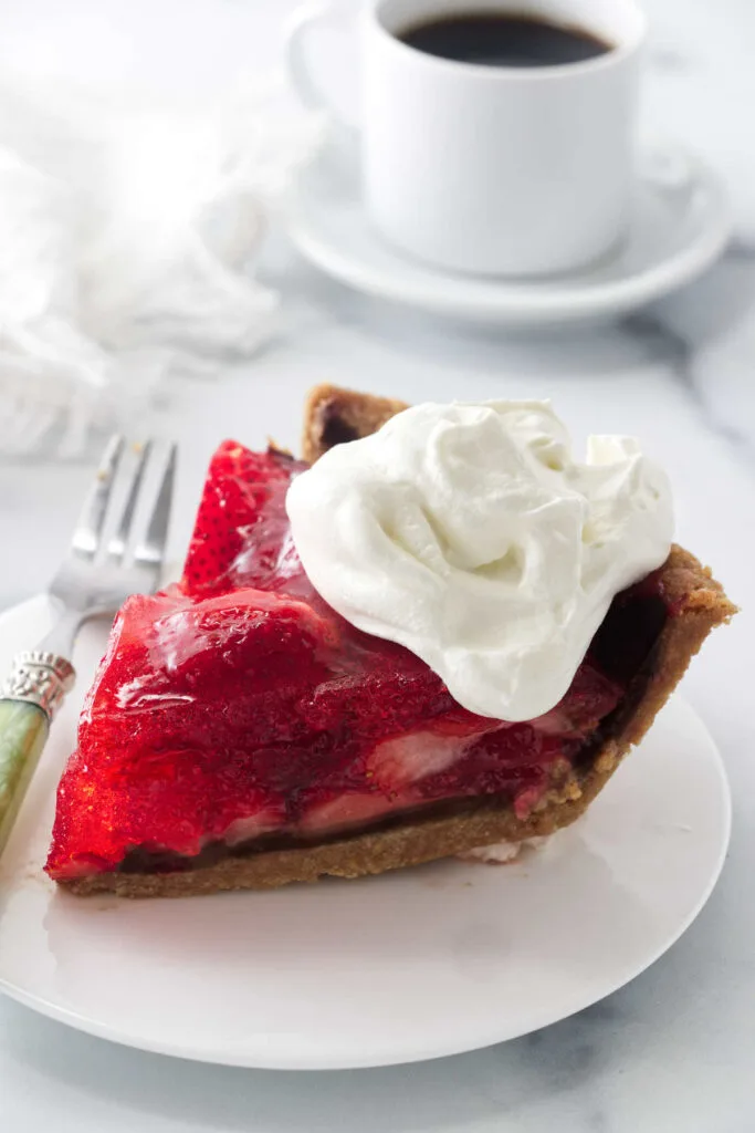 A slice of strawberry pie made with jello in front of a cup of coffee.