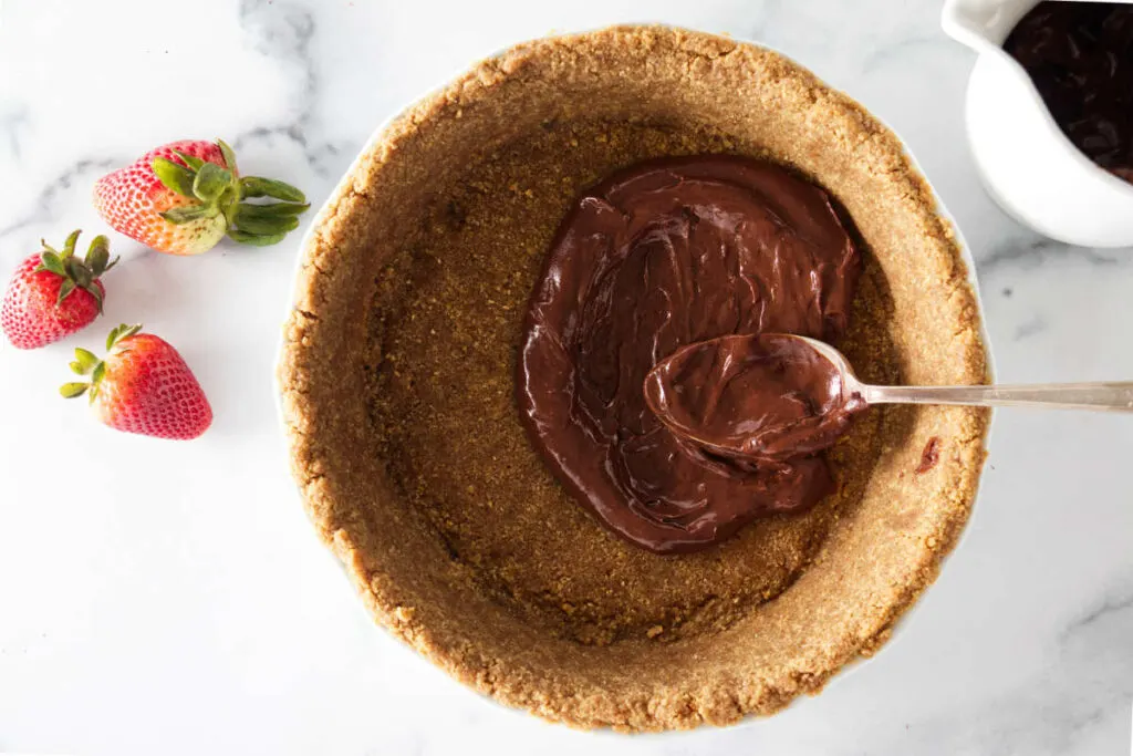 Adding chocolate ganache to a graham cracker crust.