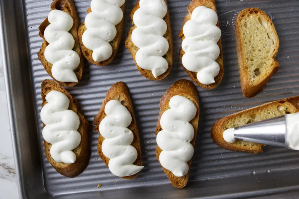 Piping whipped ricotta on top of toasted baguette slices.