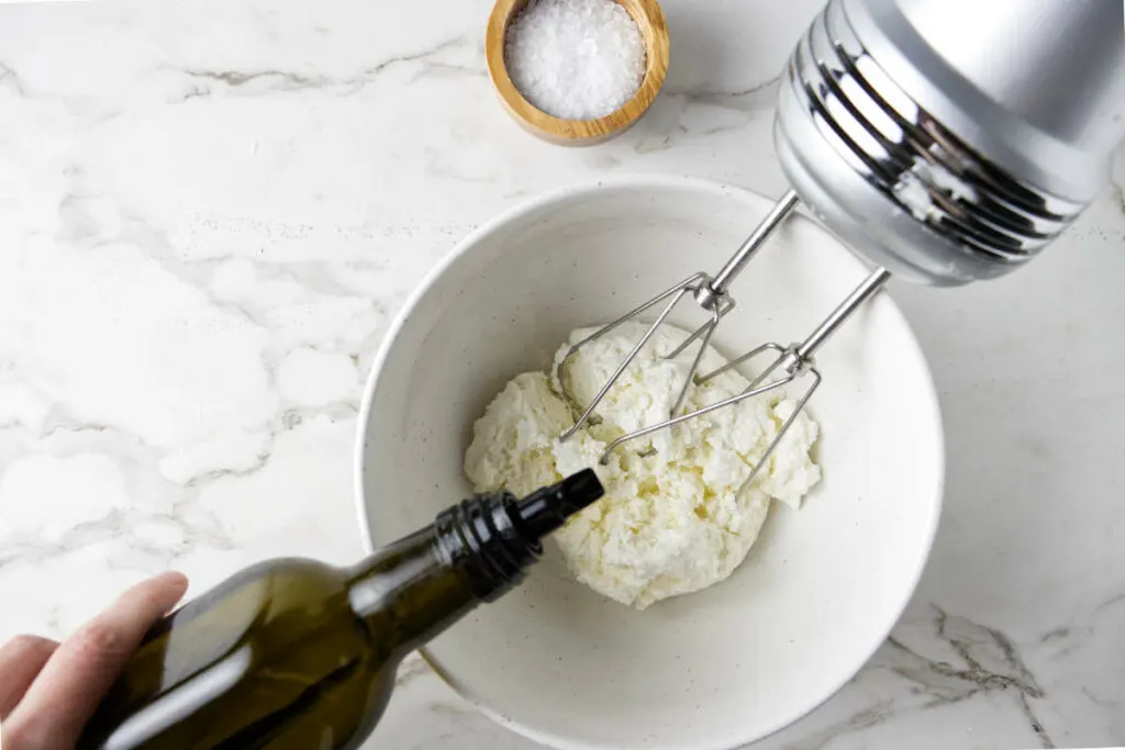 Whipping ricotta in a mixing bowl with olive oil.