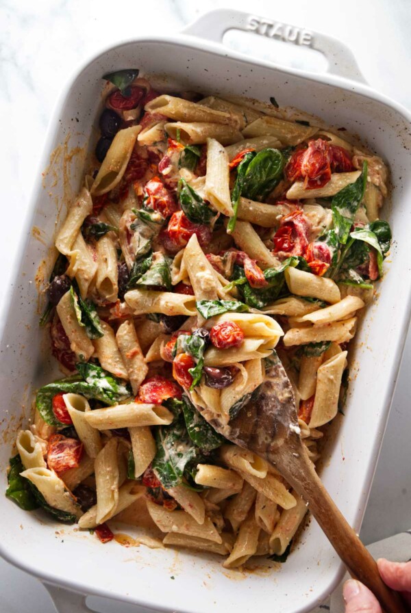 A dish of baked goat cheese pasta being tossed with a wooden spoon.