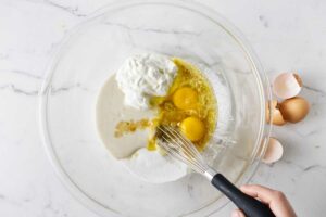 Whisking sourdough discard with eggs, sugar, butter, and sour cream.