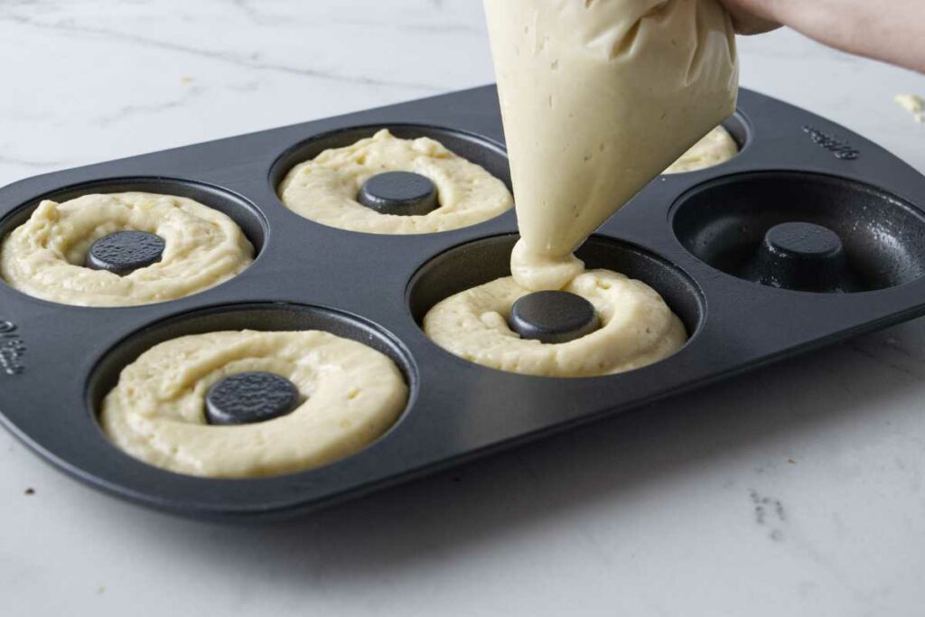 Piping the batter for sourdough discard donuts into the cavities on a donut pan.