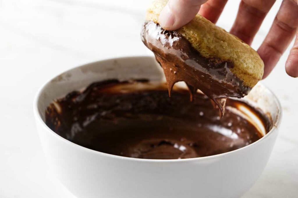 Dipping a baked donut into chocolate glaze.