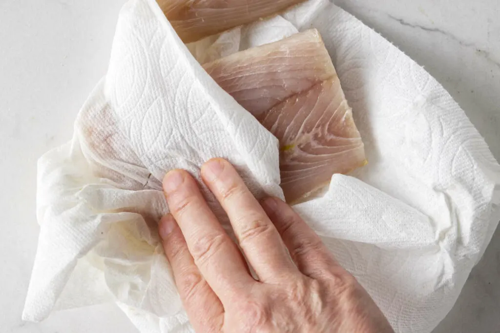 Using a paper towel to pat a filet of mahi mahi dry.