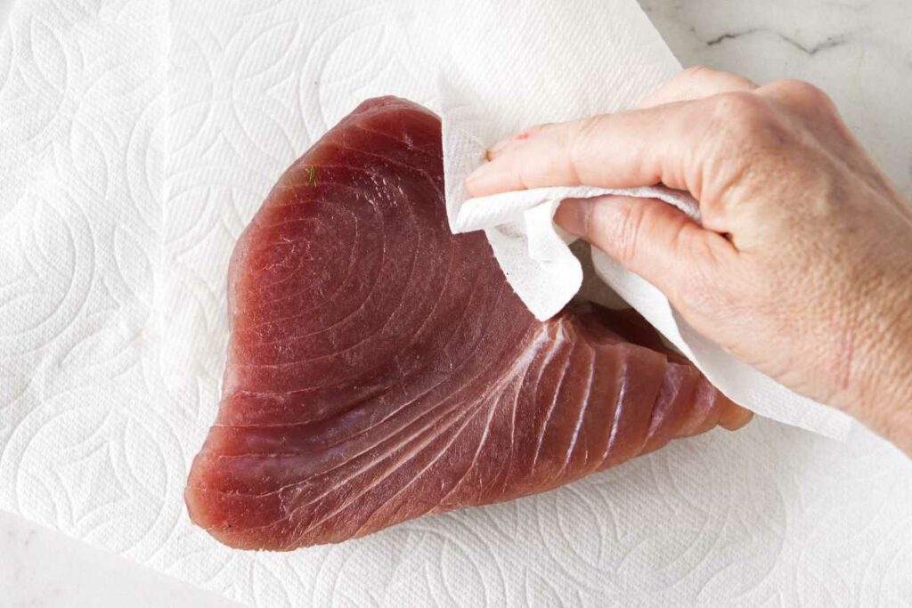 Patting a tuna steak dry with paper towels.