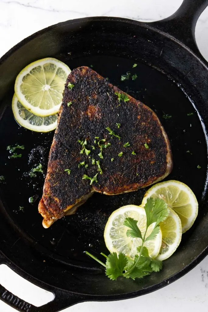 A seared tuna steak in a cast iron skillet with slices of lemon.