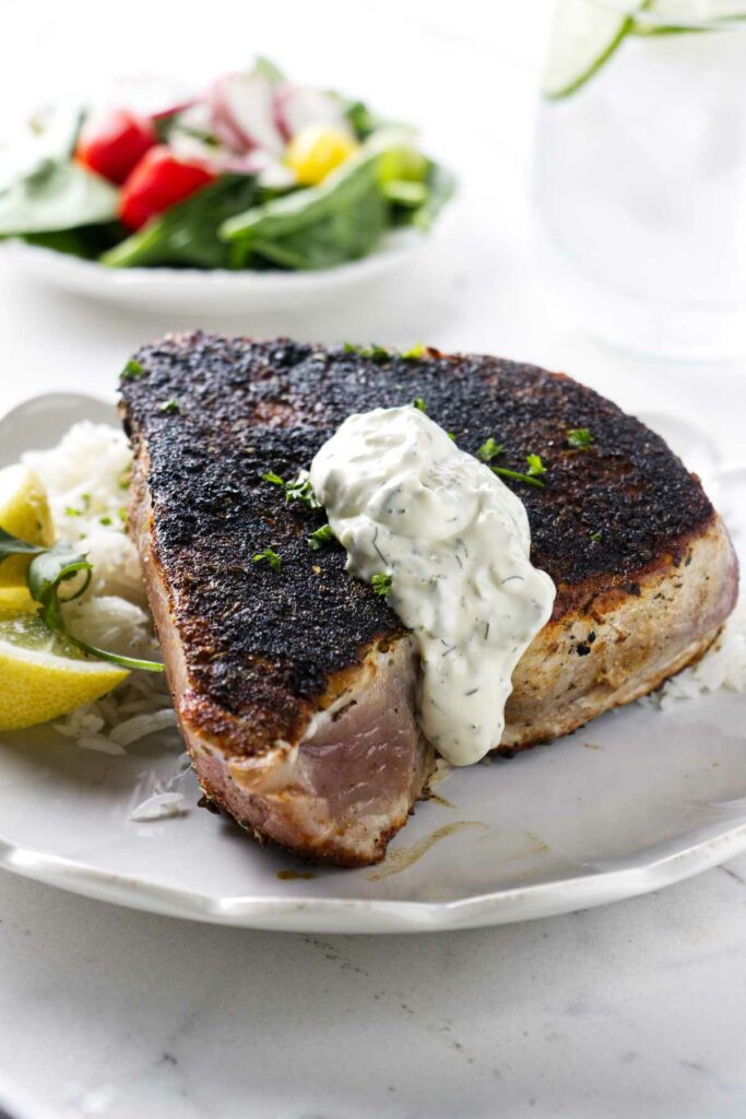 A tuna steak on a plate with lemon and rice.