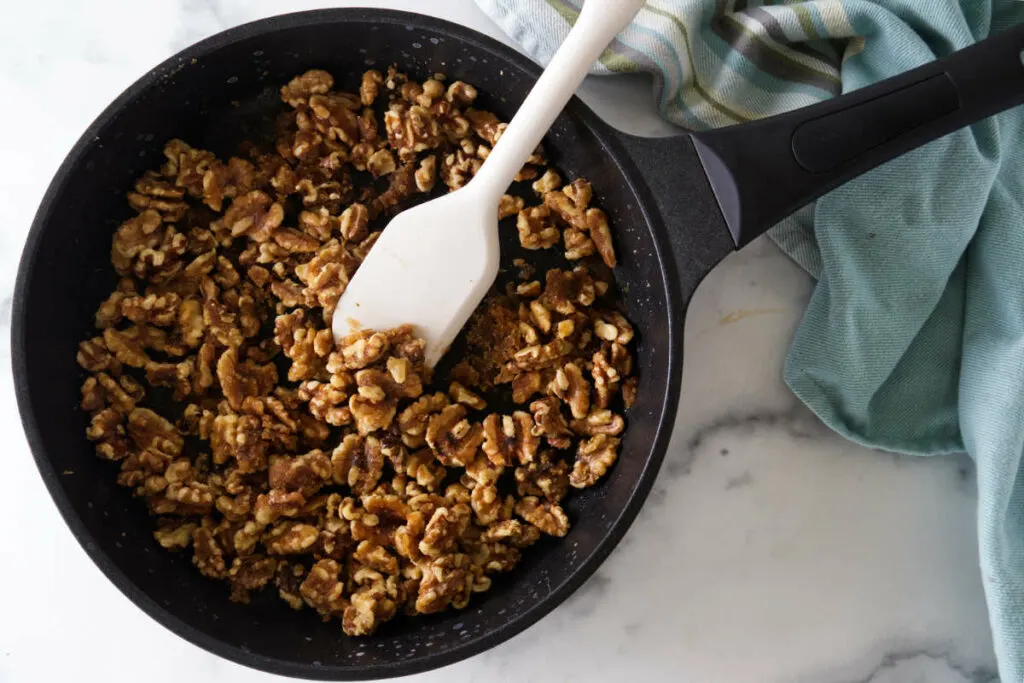 A skillet and spatula with brown sugar candied walnuts. A blue towel in the corner of the photo.