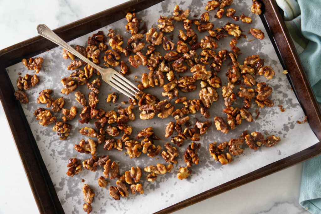 brown sugar candied walnuts on a parchment paper-lined sheet pan with a fork.