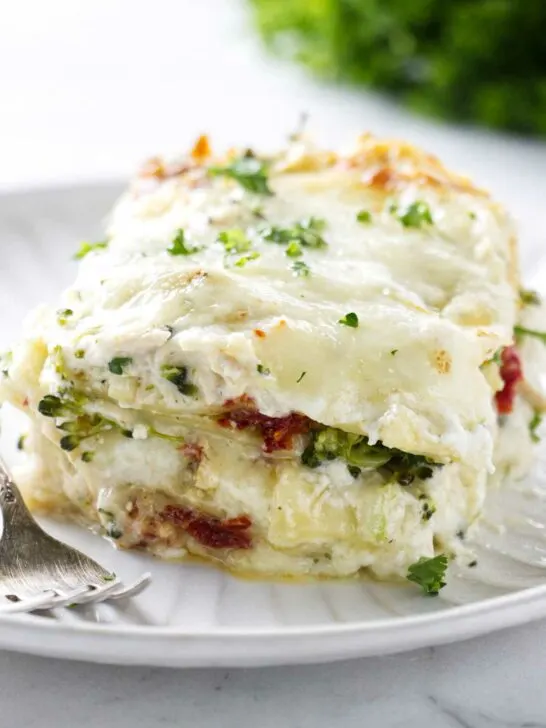A large slice of white chicken broccoli lasagna on a plate next to a fork.