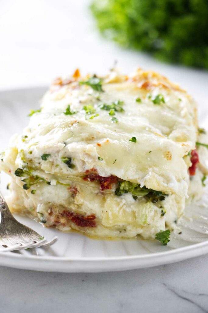A large slice of white chicken broccoli lasagna on a plate next to a fork.