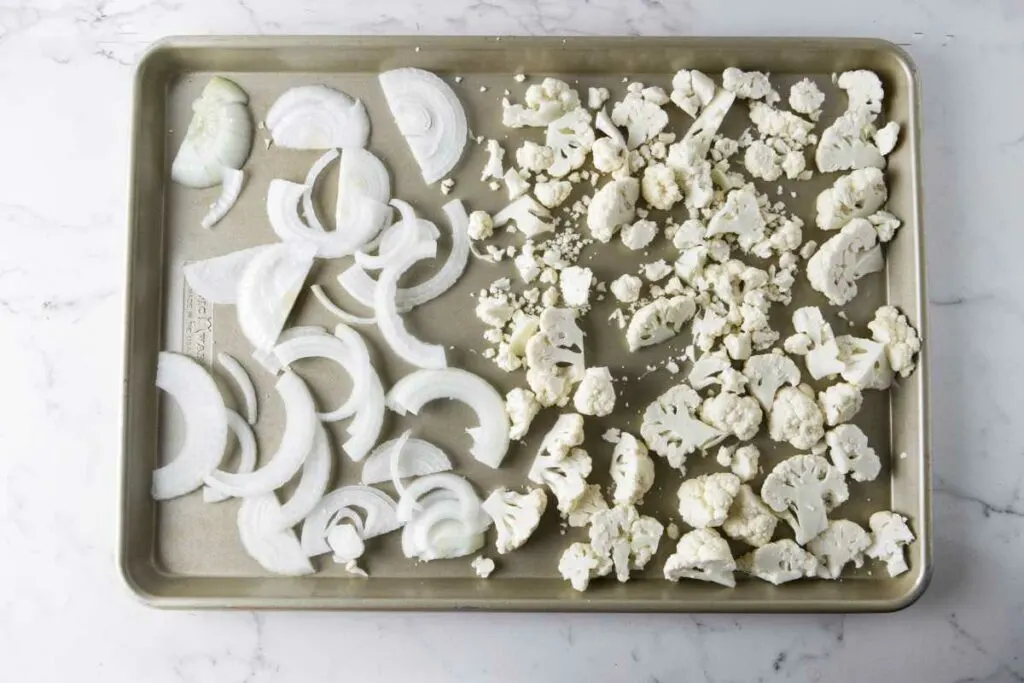 Adding onions and cauliflower to a sheet pan to roast.