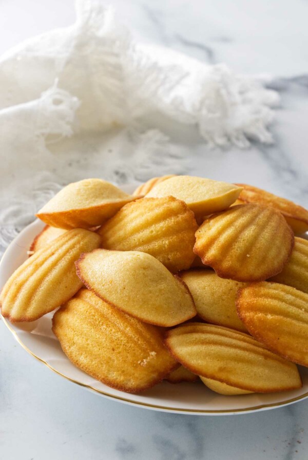A plate filled with madeleine cookies with a cloth napkin in the background.