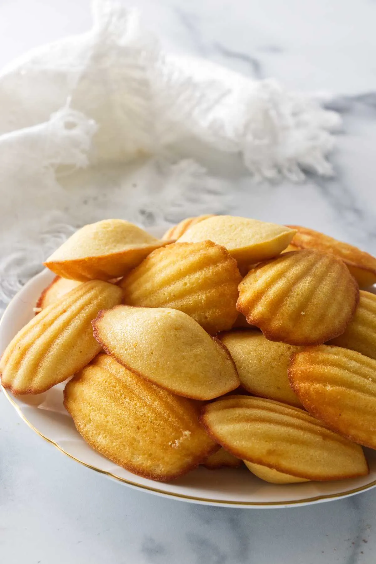 A plate filled with madeleine cookies with a cloth napkin in the background.