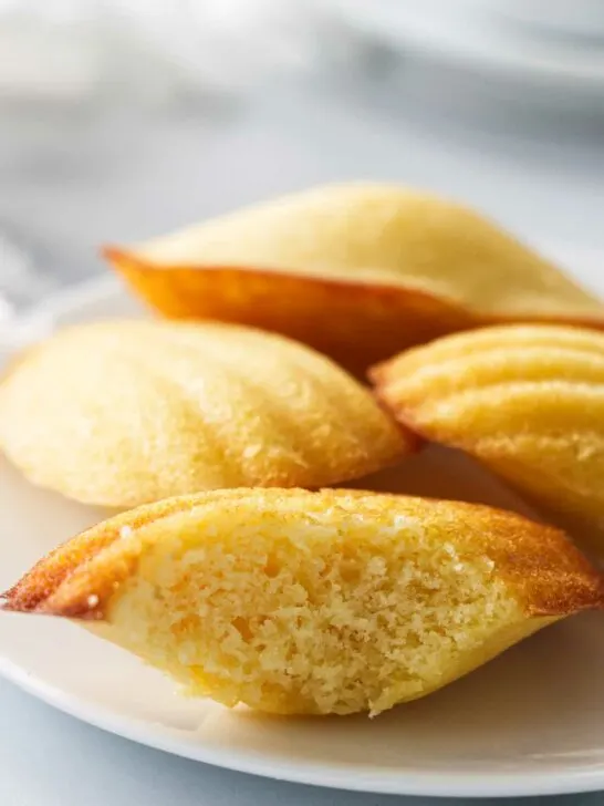 Several madeleine cakes on a plate with one of them sliced open.