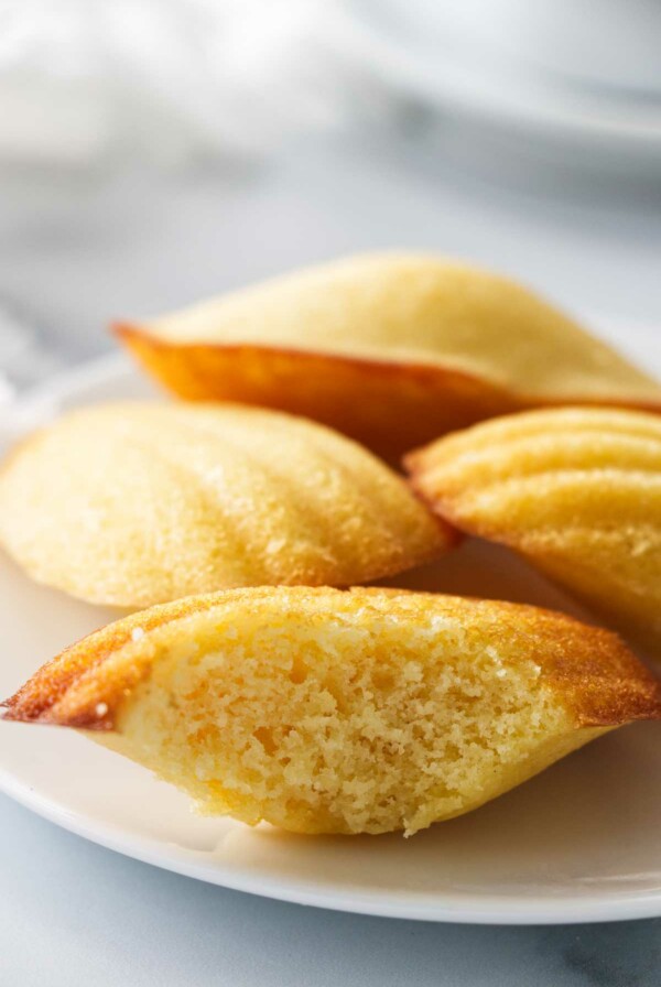 Several madeleine cakes on a plate with one of them sliced open.