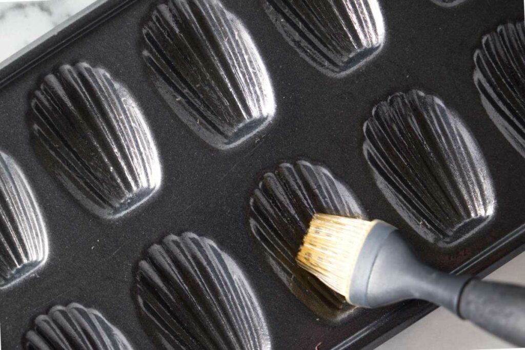 Brushing oil into the crevices of a Madeleine baking pan.