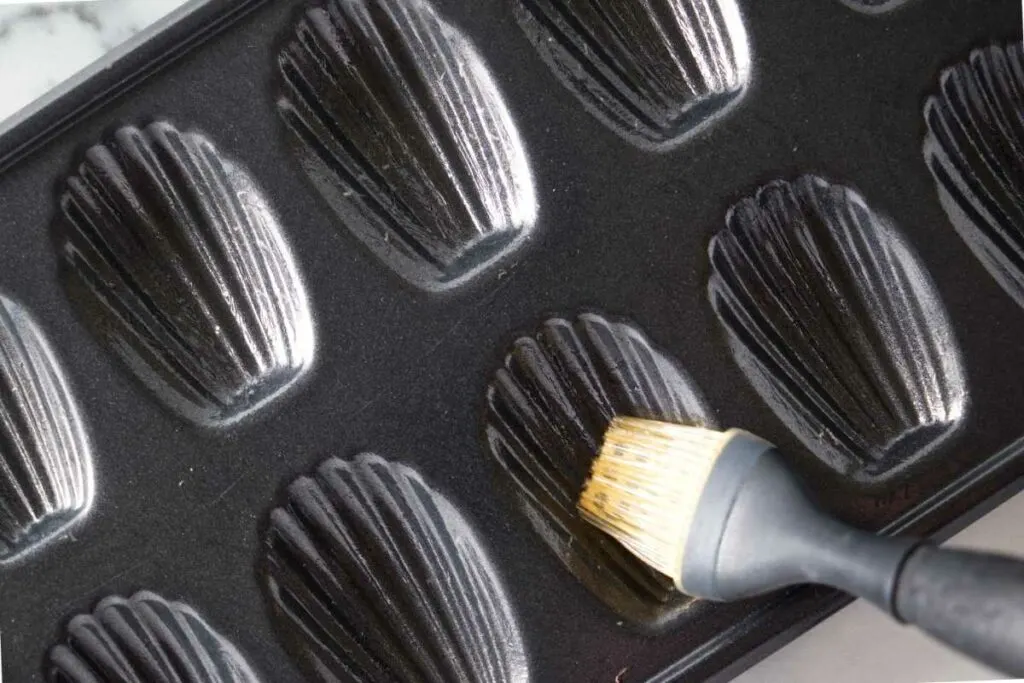 Brushing oil into the crevices of a Madeleine baking pan.