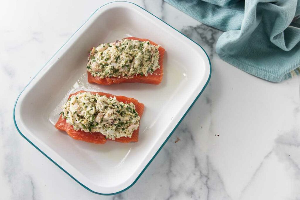 Two portions of stuffed salmon crab and shrimp in a baking pan, ready to bake.