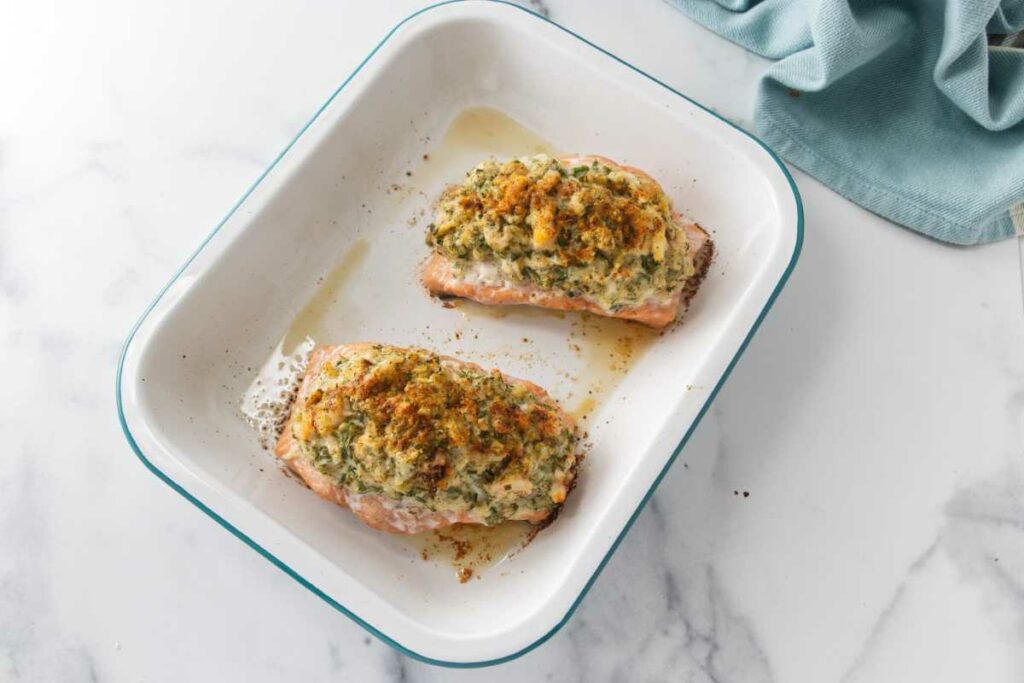 a baking pan with two baked portions of crab and shrimp stuffed salmon
