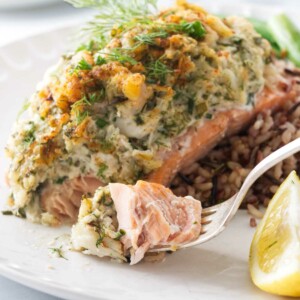A serving of crab and shrimp stuffed salmon with a bite on a fork. Salad in the background.