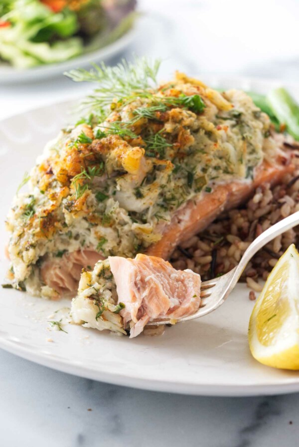 A serving of crab and shrimp stuffed salmon with a bite on a fork. Salad in the background.