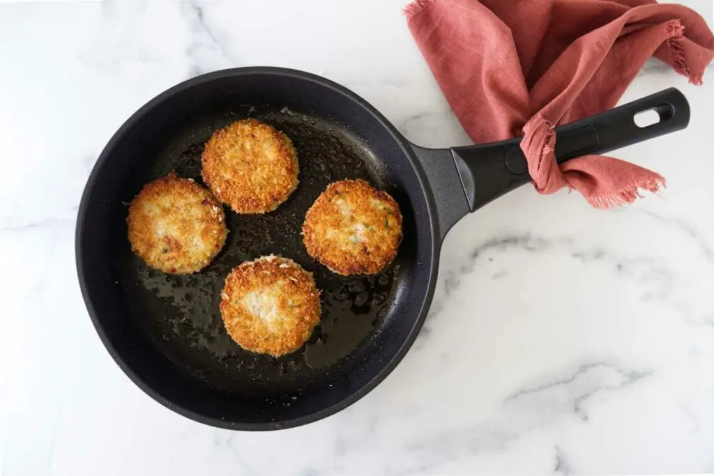 Skillet with 4 servings of cooked crab cakes.