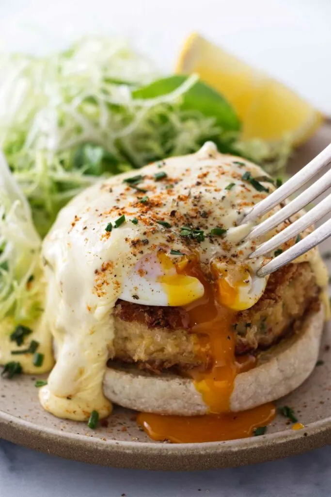 A serving of Crab Cake Benedict with a fork poking the egg.