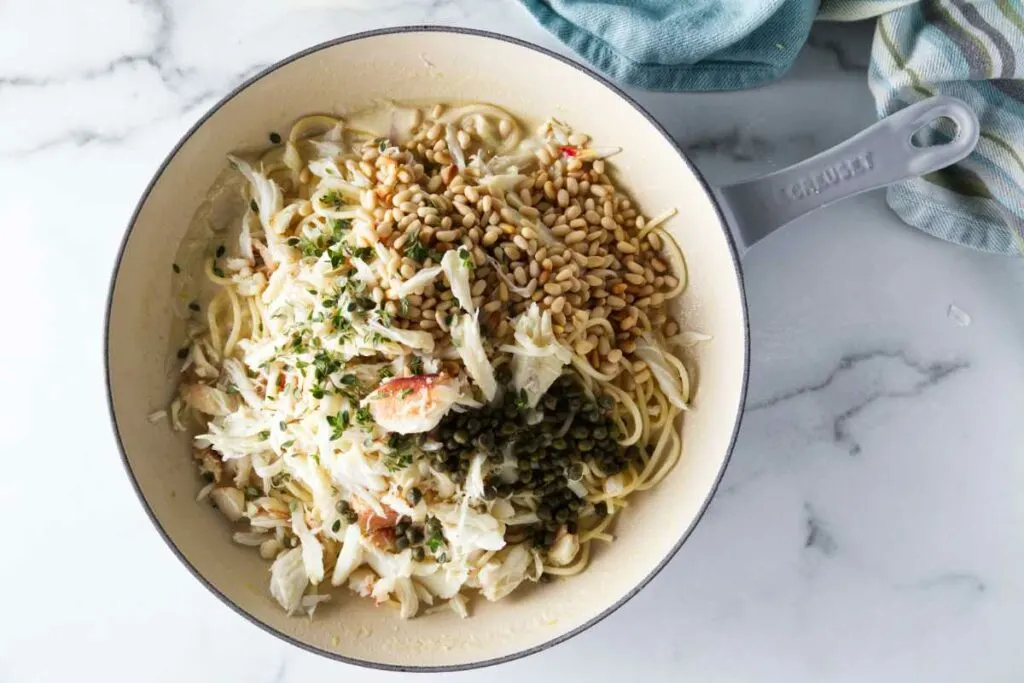 Mixing spaghetti noodles with crab, sauce, capers, and pine nuts.