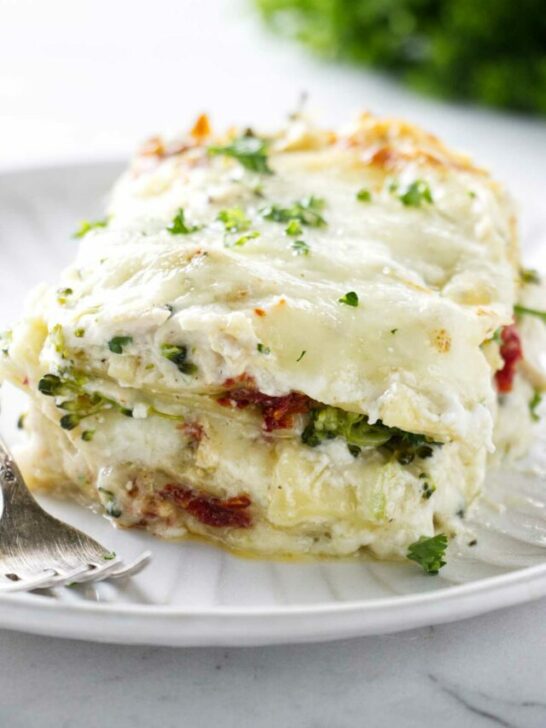 A large slice of white chicken broccoli lasagna on a plate next to a fork.