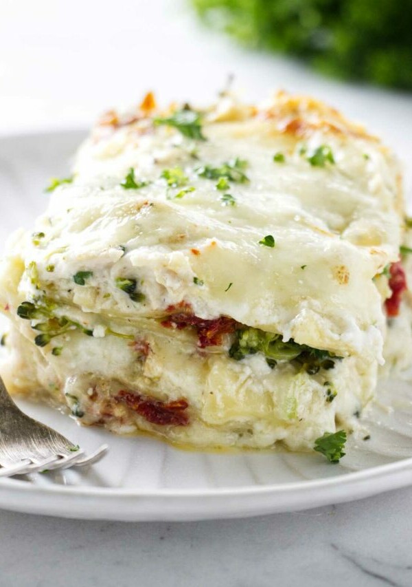 A large slice of white chicken broccoli lasagna on a plate next to a fork.