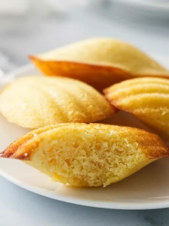 Several madeleine cakes on a plate with one of them sliced open.