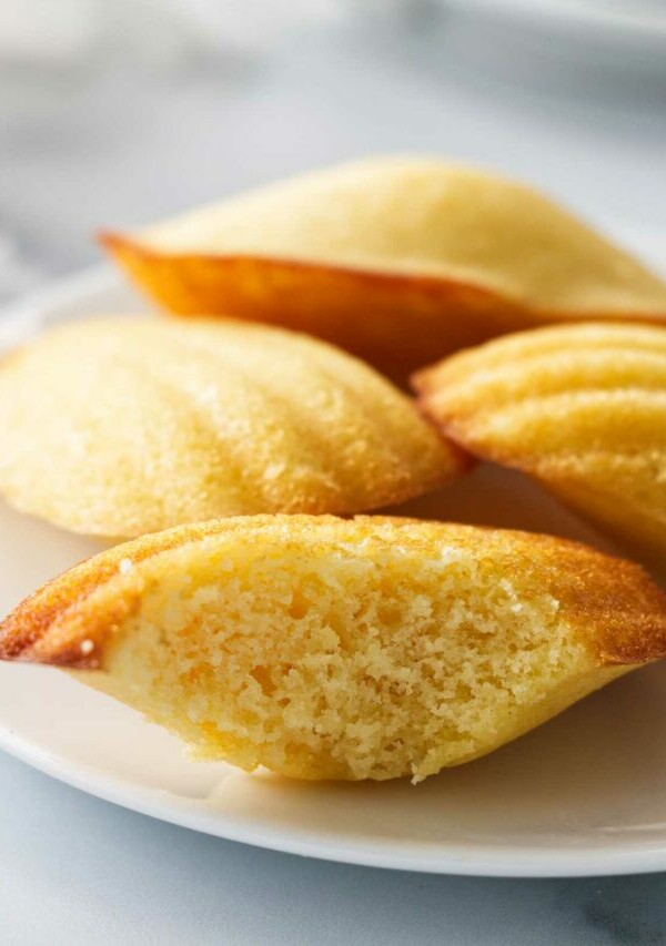 Several madeleine cakes on a plate with one of them sliced open.