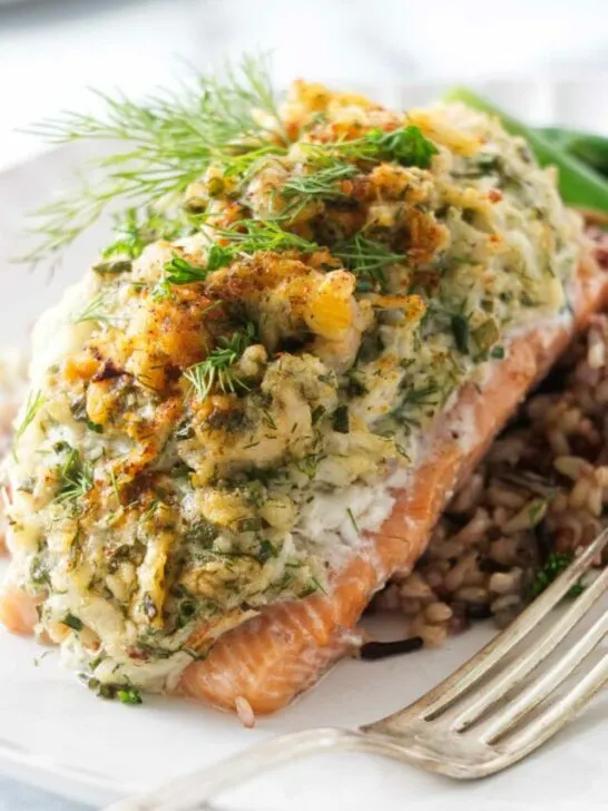 A serving of crab and shrimp stuffed salmon on a bed of wild rice blend. A fork on the plate in the foreground.