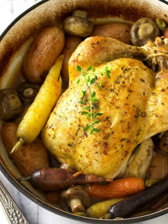 A Dutch oven whole chicken roasted with potatoes, carrots, and mushrooms.