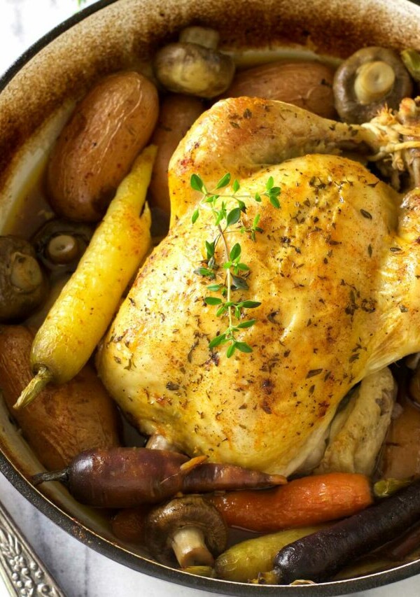 A Dutch oven whole chicken roasted with potatoes, carrots, and mushrooms.