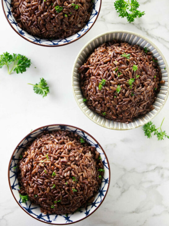 Three bowls of red rice topped with parsley.