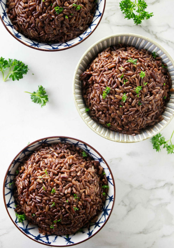 Three bowls of red rice topped with parsley.