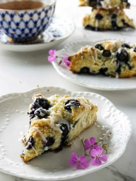 Two plates with blueberry sourdough scones next to a cup of tea.