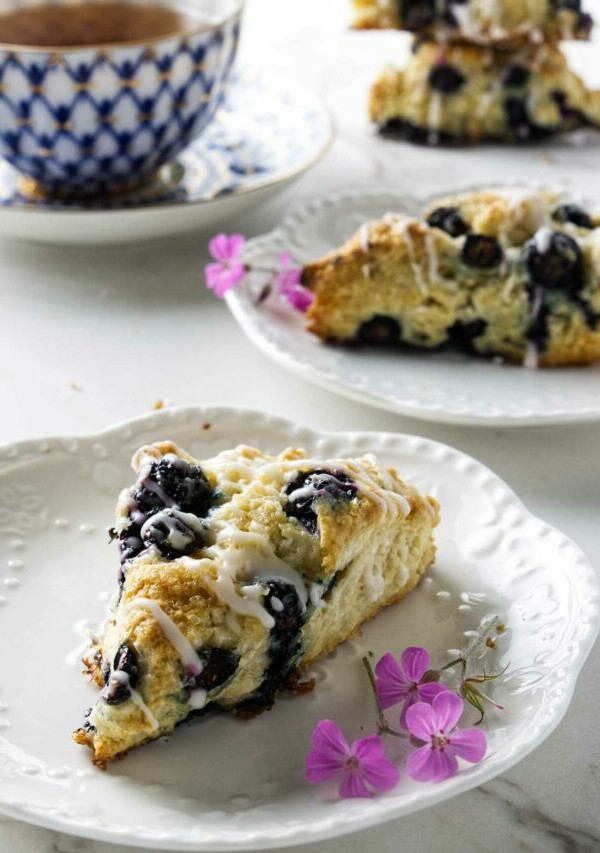 Two plates with blueberry sourdough scones next to a cup of tea.