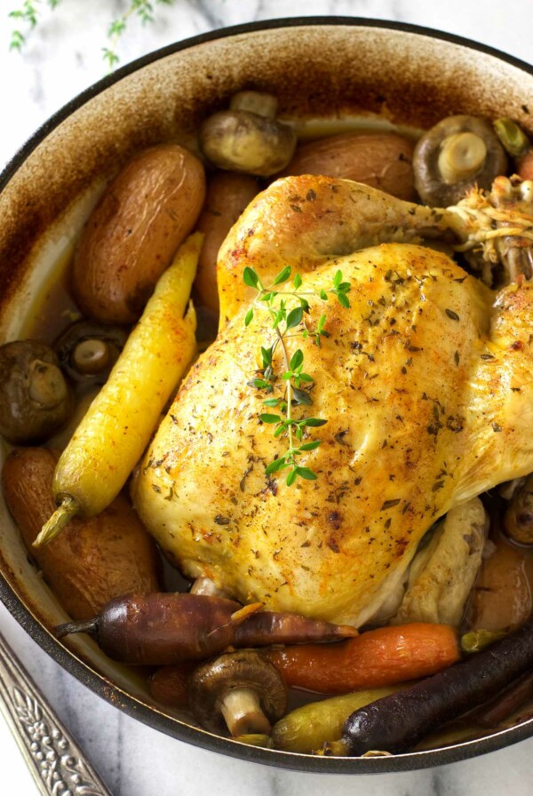 A Dutch oven whole chicken roasted with potatoes, carrots, and mushrooms.