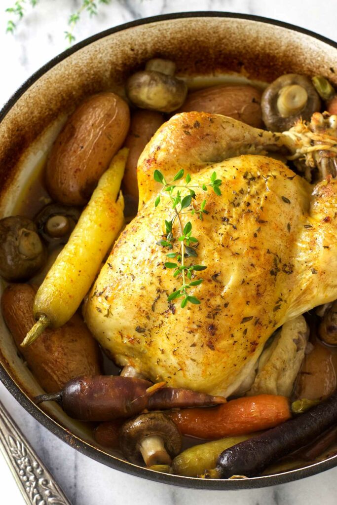 A Dutch oven whole chicken roasted with potatoes, carrots, and mushrooms.