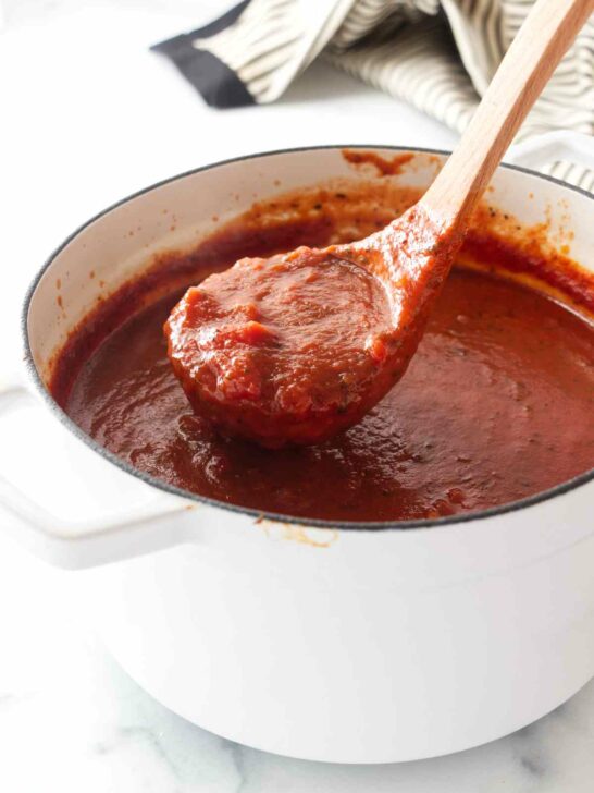A ladle scooping basil tomato sauce out of a Dutch oven.