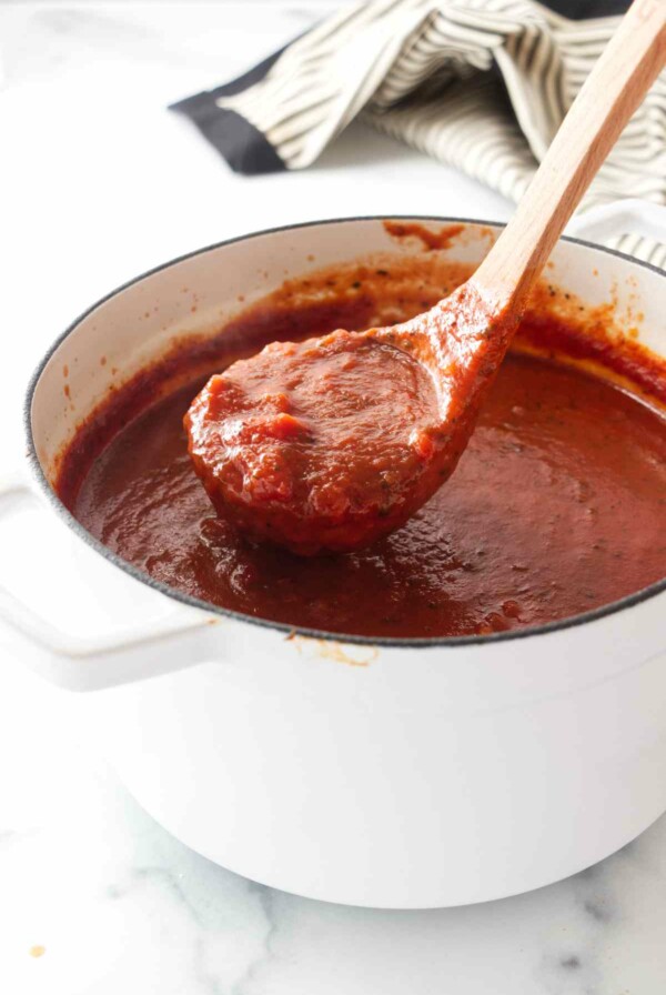 A ladle scooping basil tomato sauce out of a Dutch oven.